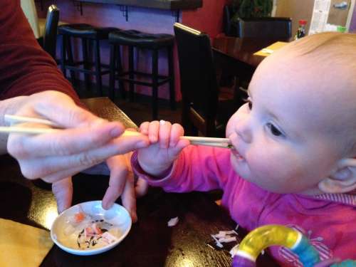 A baby eating from chopsticks for the first time.  Good times.