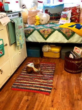 Vintage linens and lots of throw pillows make a comfy spot. A pristine 60s portable grill, too cute to use for its use, is repurposed as a magazine/book rack. A vintage tool box holds tools, while vintage luggage makes for storage and cute decor. All is “Pipsqueak” approved. 