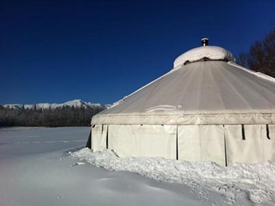 A snow-covered yurt, with Fields in the background